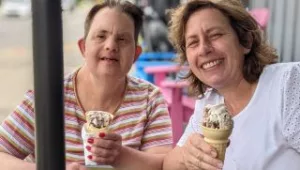 Direct Support Professional sitting with person supported at a picnic table eating icecream