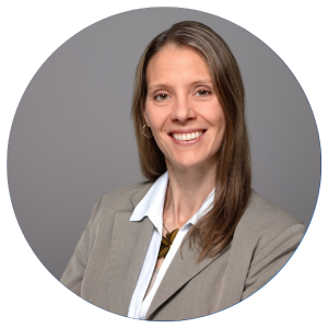 Rebecca Smith A woman with long brown hair wearing a beige blazer over a white blouse is smiling at the camera against a plain gray background.
